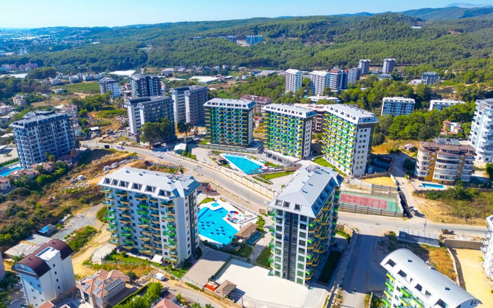 Вид с дрона на современные жилые блоки с горным и морским пейзажем в спокойном районе Аланьи. Роскошные и комфортные резиденции на побережье Средиземного моря
